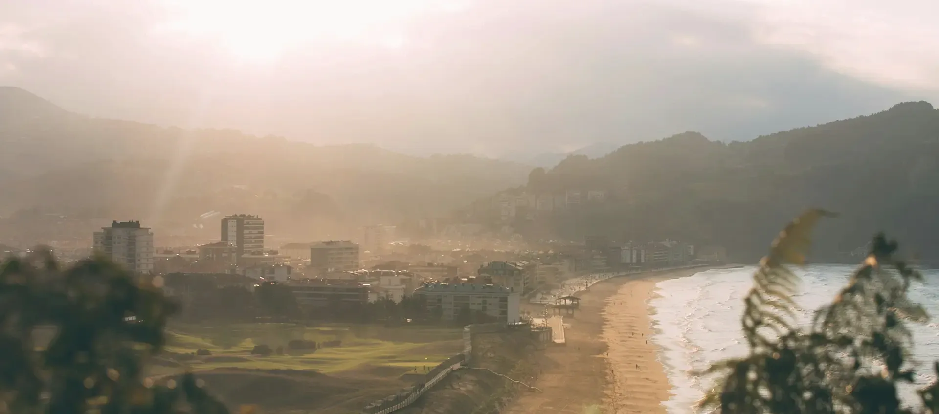 Zarautz al atardecer visto desde lo alto: la playa, el paseo marítimo y el pueblo con los montes al fondo